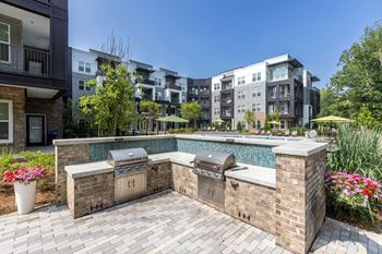 an outdoor kitchen with two grills next to a pool with an apartment building in the background at Century University City, North Carolina